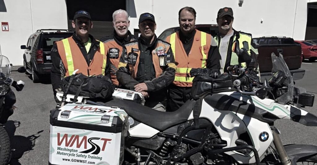5 male motorcycle instructors standing behind a white motorcycle