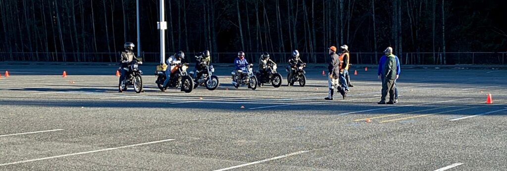 motorcycle students learning to ride are lined up with motorcycle instructors helping them