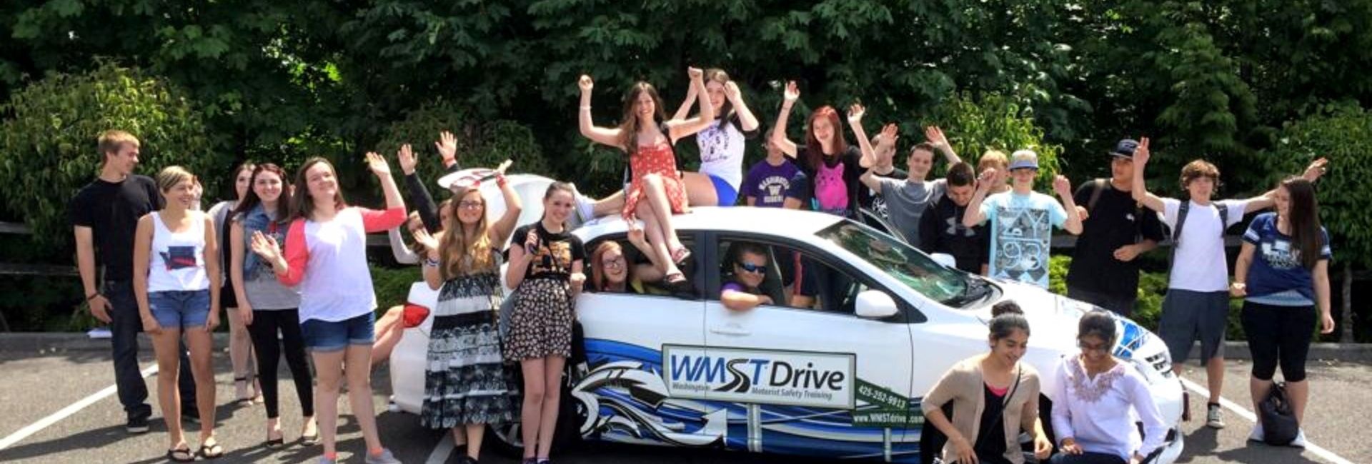 mariner high school drivers ed students sitting on a white drive car smiling and waving
